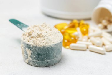 Beyaz kaşıkta beyaz protein tozu, beyaz amino asit kapsülleri, vitaminler ve sarı kapsüller beyaz arka planda Omega 3, sağlıklı beslenme ve vücut geliştirme besinleri..