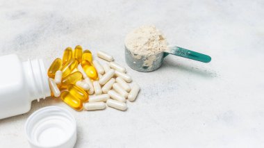 Beyaz kaşıkta beyaz protein tozu, beyaz amino asit kapsülleri, vitaminler ve sarı kapsüller beyaz arka planda Omega 3, sağlıklı beslenme ve vücut geliştirme besinleri..