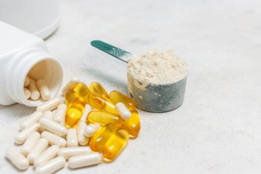 Beyaz kaşıkta beyaz protein tozu, beyaz amino asit kapsülleri, vitaminler ve sarı kapsüller beyaz arka planda Omega 3, sağlıklı beslenme ve vücut geliştirme besinleri..