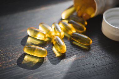 Omega 3 balık yağı sarı kapsüller, koyu ahşap tahtada beslenme takviyesi, sağlıklı beslenme konsepti, yakın görüş..