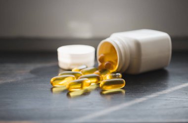 Omega 3 balık yağı sarı kapsüller, koyu ahşap tahtada beslenme takviyesi, sağlıklı beslenme konsepti, yakın görüş..