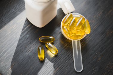 Omega 3 balık yağı sarı kapsüller plastik bir kaşık içinde, diyet takviyesi koyu ahşap tahta üzerinde, sağlıklı beslenme konsepti, yakın görüş.