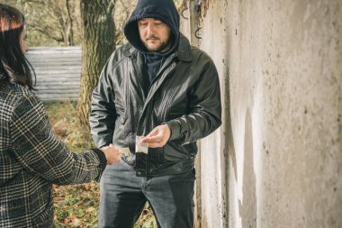 Erkek uyuşturucu satıcısı, açık havada, elinde parası olan bağımlı bir kadına şeffaf plastik poşet içinde sert uyuşturucu satıyor..