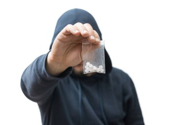 Kapüşonlu suçlu şeffaf plastik torba tutuyor. Beyaz arka planda izole edilmiş sert haplar, uyuşturucu satıcısı veya gangster uyuşturucu satıyor..