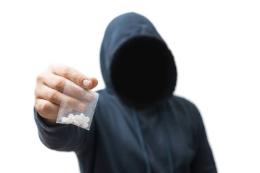Kapüşonlu meçhul bir adam şeffaf plastik torba tutuyor. Beyaz arka planda izole edilmiş sert haplar var. Uyuşturucu satıcısı ya da gangster uyuşturucu satıyor..