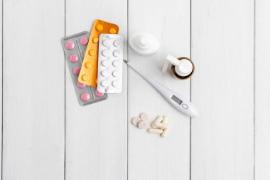 Soğuk algınlığı ilaçları, ilaçlar, termometre, kapsüller ve haplar ahşap masadaki su toplayan bir pakette. Sağlık konsepti, evde grip ve koronavirüs tedavisi..