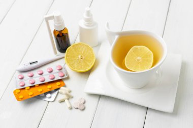 Limonlu çay fincanı, soğuk algınlığı ilacı, termometre, kapsüller ve haplar ahşap bir masada su toplamış. Ev tedavisi grip ve koronavirüs kavramı.