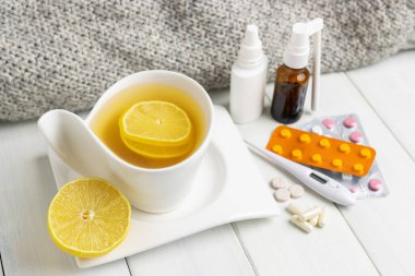 Limonlu çay fincanı, soğuk algınlığı ilacı, termometre, kapsüller ve haplar ahşap bir masada su toplamış. Ev tedavisi grip ve koronavirüs kavramı.