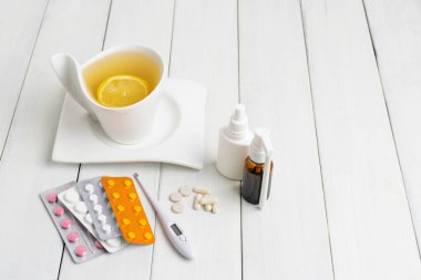 Limonlu çay fincanı, soğuk algınlığı ilacı, termometre, kapsüller ve haplar ahşap bir masada su toplamış. Ev tedavisi grip ve koronavirüs kavramı.