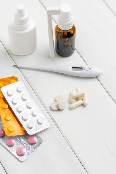 Cold remedies, medicines, thermometer, capsules and pills in a blister pack on wooden table. Healthcare concept, home treatment of flu and coronavirus.
