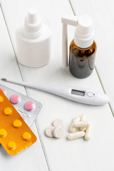 Cold remedies, medicines, thermometer, capsules and pills in a blister pack on wooden table. Healthcare concept, home treatment of flu and coronavirus.