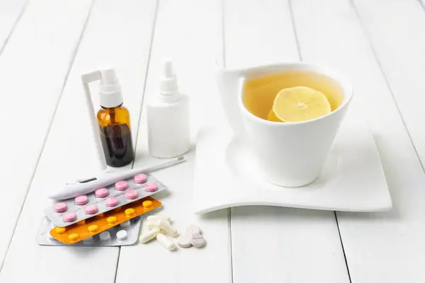 Tea cup with lemon, cold remedies, medicine, thermometer, capsules and pills in a blister pack on wooden table. Concept of home treatment flu and coronavirus.