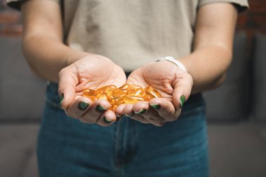 Genç kadın elinde omega-3 balık yağı, vitamin sarısı kapsüller, yakın çekim görüntüler tutuyor..