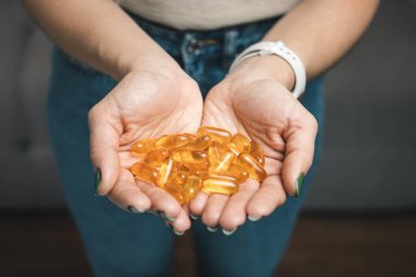 Genç kadın elinde omega-3 balık yağı, vitamin sarısı kapsüller, yakın çekim görüntüler tutuyor..