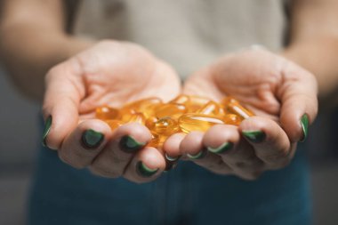 Genç kadın elinde omega-3 balık yağı, vitamin sarısı kapsüller, yakın çekim görüntüler tutuyor..