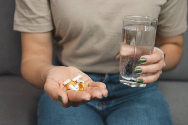 Genç bir kadın elinde çeşitli ilaç ve kapsüller tutuyor. Bir bardak su, yakın çekim..