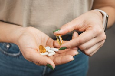 Genç bir kadın bir kapsül Omega 3 takviyesi alır ve çeşitli ilaç ve kapsülleri yakın çekimde elinde tutar..