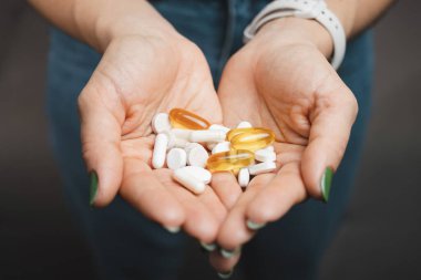 Genç bir kadın, çeşitli ilaç ve kapsüllerden oluşan yığını elinde tutuyor..