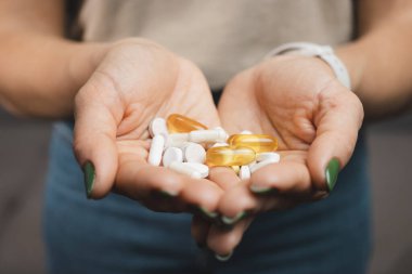 Genç bir kadın, çeşitli ilaç ve kapsüllerden oluşan yığını elinde tutuyor..