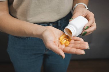 Genç kadın elinde omega 3 kapsülü tutuyor, dişi balık yağı takviyesi alıyor ve vitaminleri şişeden alıyor, yakın plan görüntüden..