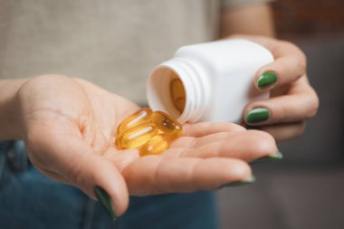 Genç kadın elinde omega 3 kapsülü tutuyor, dişi balık yağı takviyesi alıyor ve vitaminleri şişeden alıyor, yakın plan görüntüden..