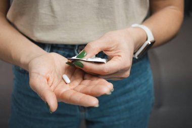 Genç bir kadın elinde beyaz hap tutuyor, su toplamış paketten ilaç alıyor, yakından bakıyor..