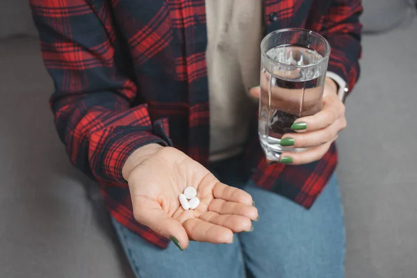 Young woman takes a medicine, holds in a hand white pills and glass of water, close-up view.