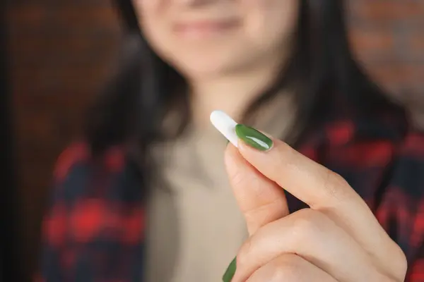 Young woman takes a medicine, holds white pill in a hand, close-up view.