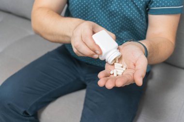 Şişeden ilaç alan bir adam, elinde beyaz tedavi kapsülleri, antibiyotikler, vitaminler, ağrı kesici haplar, yakın çekim görüntüsü....