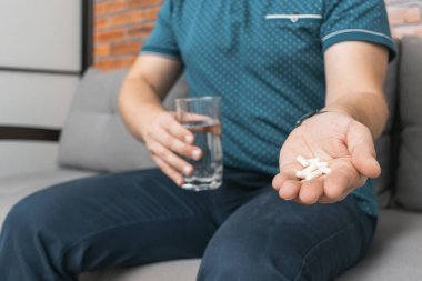 İlaç alan bir adam, elinde beyaz terapi hapları, antibiyotikler, ağrı kesici ve bir bardak su, yakın çekim..
