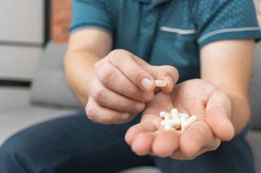 Şişeden ilaç alan bir adam, elinde beyaz tedavi kapsülleri, antibiyotikler, vitaminler, ağrı kesici haplar, yakın çekim görüntüsü....