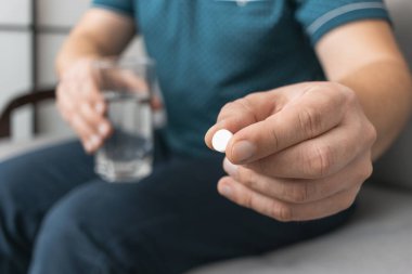 İlaç alan bir adam, elinde beyaz terapi hapı, antibiyotik, ağrı kesici ve bir bardak su ile yakın çekim görüntüsü olan.