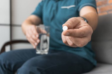 İlaç alan bir adam, elinde beyaz terapi hapı, antibiyotik, ağrı kesici ve bir bardak su ile yakın çekim görüntüsü olan.