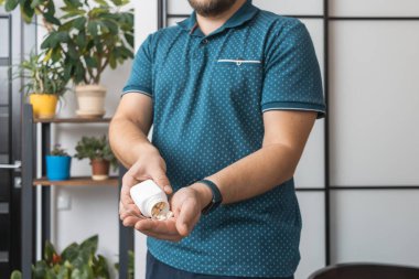 Şişeden ilaç alan bir adam, elinde beyaz tedavi kapsülleri, antibiyotikler, vitaminler, ağrı kesici haplar, yakın çekim görüntüsü....