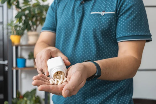 Şişeden ilaç alan bir adam, elinde beyaz tedavi kapsülleri, antibiyotikler, vitaminler, ağrı kesici haplar, yakın çekim görüntüsü....
