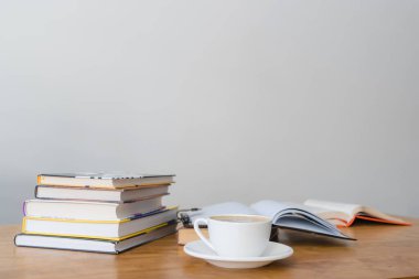 Bir fincan sıcak kahve, açık kitap ve ahşap masa üzerinde kitap yığını, ön plana odaklan.
