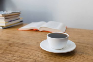 Bir fincan sıcak kahve, açık kitap ve ahşap masa üzerinde kitap yığını, ön plana odaklan.