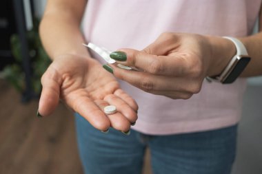 Elinde hap tutan genç bir kadın, ağrı kesici ya da antibiyotik, su toplayan paketten ilaç alıyor, yakından bakıyor..