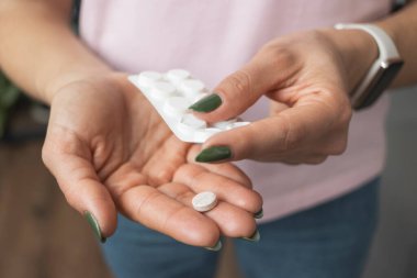 Elinde hap tutan genç bir kadın, ağrı kesici ya da antibiyotik, su toplayan paketten ilaç alıyor, yakından bakıyor..