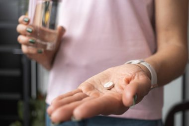 İlaç, ağrı kesici ya da antibiyotik alan genç bir kadın elinde bir bardak su tutuyor.