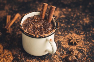 Tarçın çubuklu ev yapımı acılı sıcak çikolata, yıldız anason, koyu arka planda diş mineli çikolata, kakao tozu ve çikolata parçacıkları..