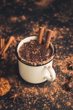 Tarçın çubuklu ev yapımı acılı sıcak çikolata, yıldız anason, koyu arka planda diş mineli çikolata, kakao tozu ve çikolata parçacıkları..