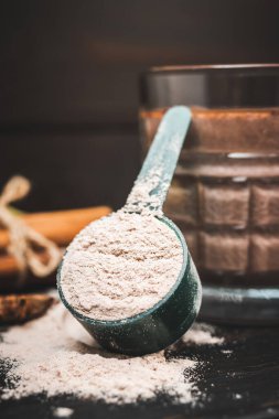 Beyaz protein tozu koyu ahşap tahta üzerinde kaşık ölçme tozu ile bir bardak milkshake smoothie içecek, muz, yıldız anason, badem, tarçın çubuğu, çikolata parçaları..