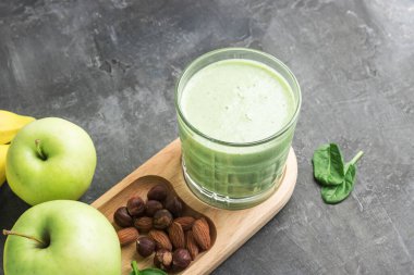 Bardakta yeşil detoks smoothie, ıspanak yaprakları, elma, muz ve fındık karışımı koyu arka planda sağlıklı beslenme konsepti..