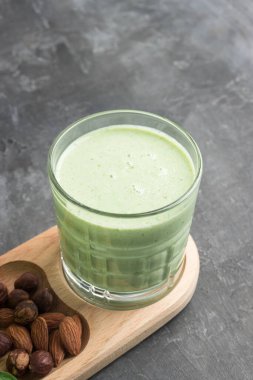 Bardakta yeşil detoks smoothie, ıspanak yaprakları, elma, muz ve fındık karışımı koyu arka planda sağlıklı beslenme konsepti..