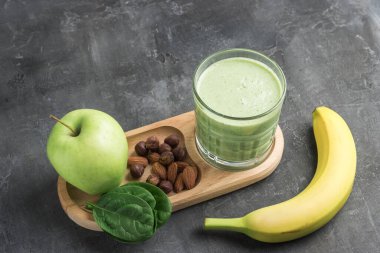 Bardakta yeşil detoks smoothie, ıspanak yaprakları, elma, muz ve fındık karışımı koyu arka planda sağlıklı beslenme konsepti..