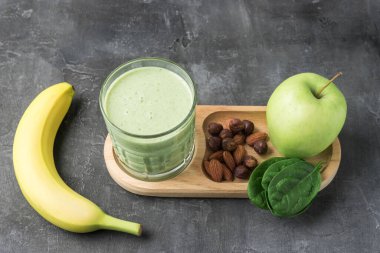 Bardakta yeşil detoks smoothie, ıspanak yaprakları, elma, muz ve fındık karışımı koyu arka planda sağlıklı beslenme konsepti..