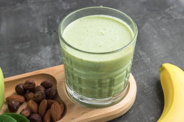 Bardakta yeşil detoks smoothie, ıspanak yaprakları, elma, muz ve fındık karışımı koyu arka planda sağlıklı beslenme konsepti..