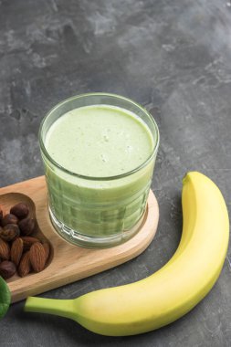 Bardakta yeşil detoks smoothie, ıspanak yaprakları, elma, muz ve fındık karışımı koyu arka planda sağlıklı beslenme konsepti..
