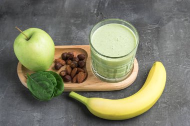 Bardakta yeşil detoks smoothie, ıspanak yaprakları, elma, muz ve fındık karışımı koyu arka planda sağlıklı beslenme konsepti..